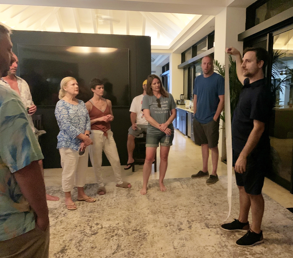 Dario is holding a piece of paper showing the scale of the solar system to attendees of a wedding gathered in a circle around him