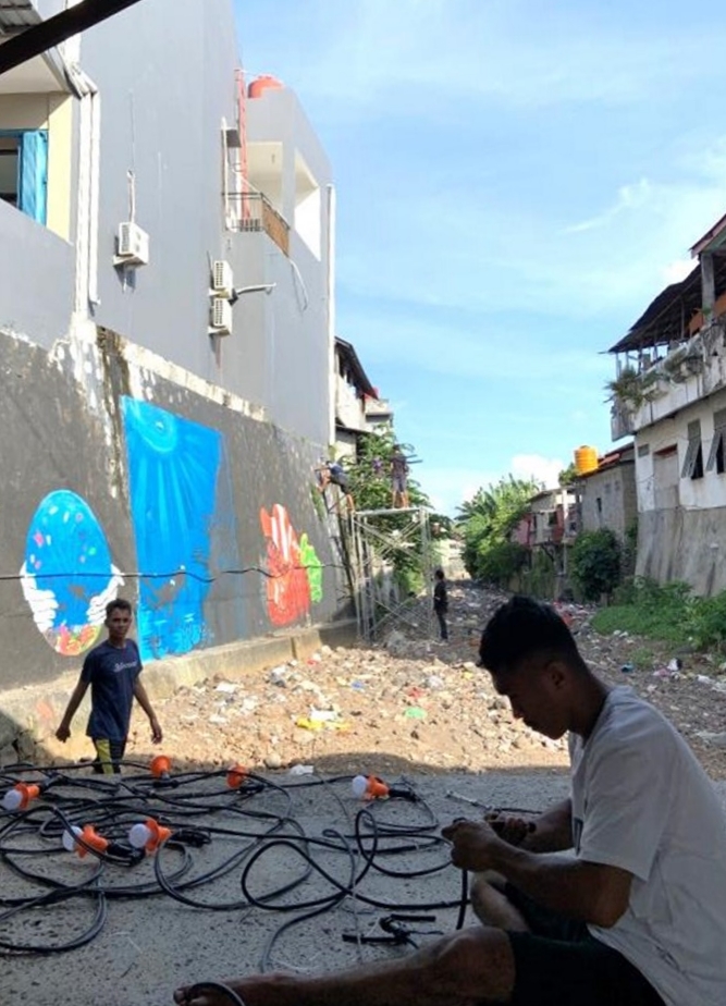 Two people working on a long string of wires with lights in the canal in front of murals showing ocean life and scuba divers