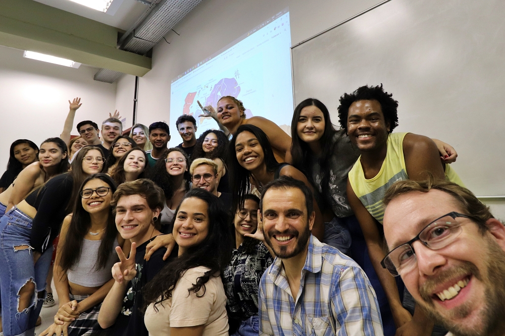 Group of multi-cultural students with two professors in lower corner, with map of South American-type continent projected behind them