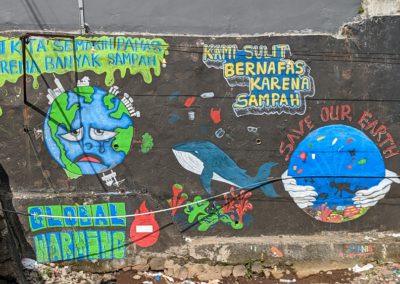 A view of the canal mural, showing an unhappy sweating Earth, a whale swimming in garbage, and hands holding an ocean setting with the words "Save our Earth"