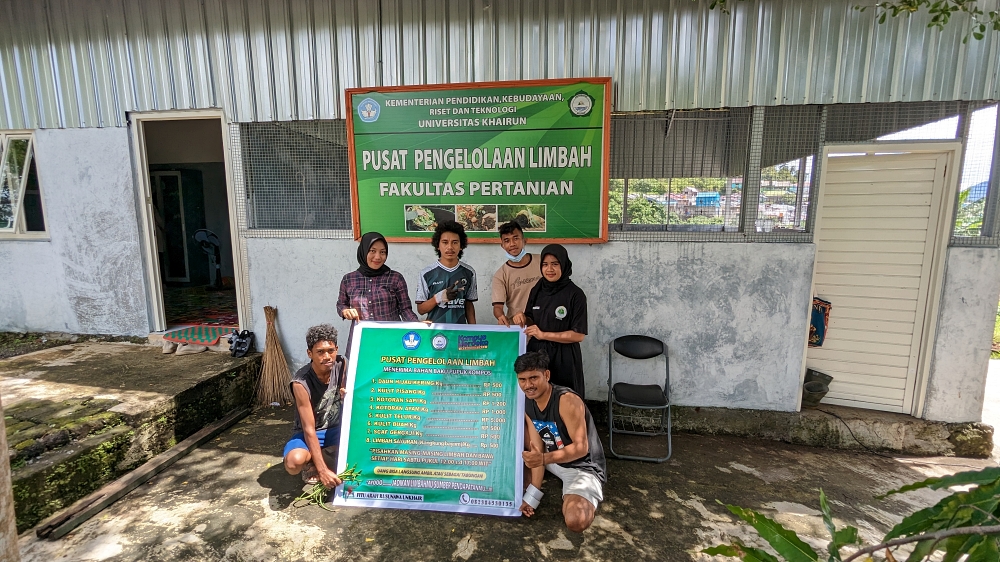 Six students hold a sign showing how much they'll pay for organic waste in front of a building for composting with the signage "Pusat Pengelolaan Limbah, Fakultas Pertanian"