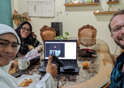 Two women in hijabs (Lily and Mar) on the left of a laptop logged into Zoom, with Lev to the right