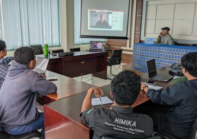 Five Indonesian students sitting at desks in front of a screen showing the image of a student in Ukraine