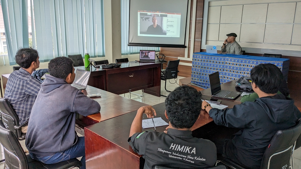 Five Indonesian students sitting at desks in front of a screen showing the image of a student in Ukraine