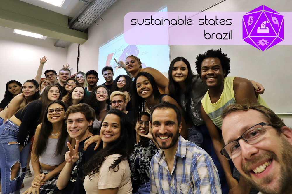 A group of multi-ethnic students and professors smiling in a group in front of a projected map of the fictional continent of Toltecan, which resembles South America