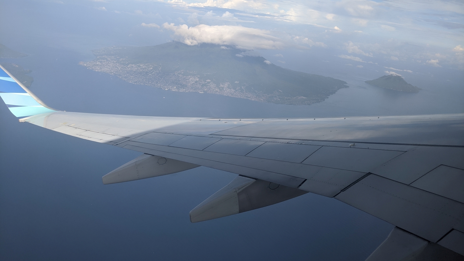 Airplane wing framing a volcanic island with a dense city at the base