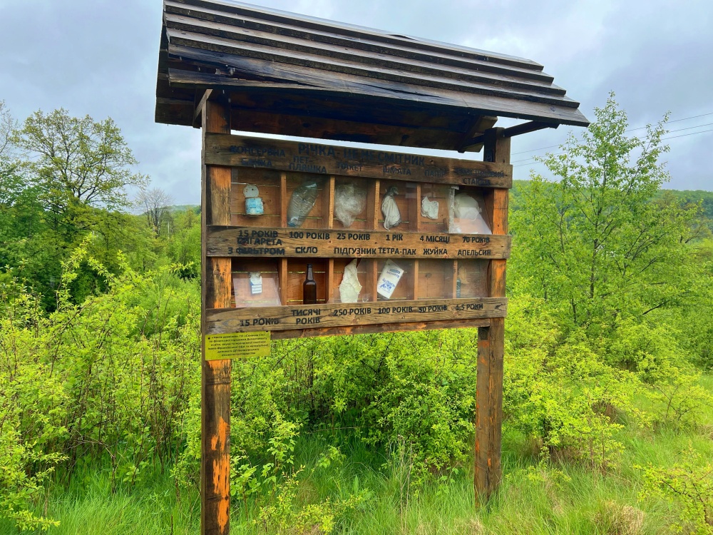 Ecotourism Exhibit Wooden panel with roofing and multiple alcoves with glass, paper, tin cans, and other garbage and the amount of time it would take the garbage to degrade in the environment