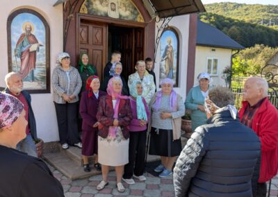 A group of elderly women in colorful headscarves and Sunday clothing standing in front of an Eastern Rite Greco-Catholic church speaking with two older professors