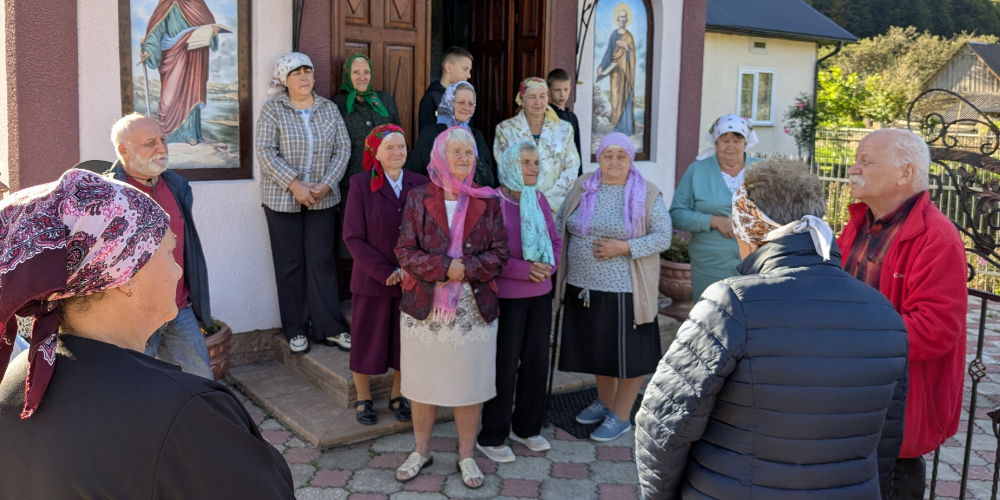 A group of elderly women in colorful headscarves and Sunday clothing standing in front of an Eastern Rite Greco-Catholic church speaking with two older professors