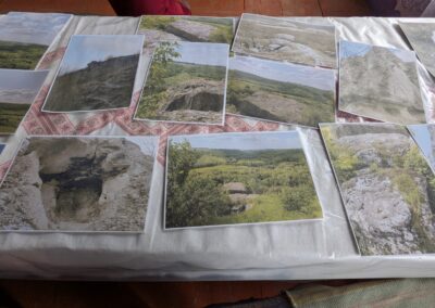 A series of photographs of grey rock outcrops in a green forest laid out on a table with an embroidered tablecloth